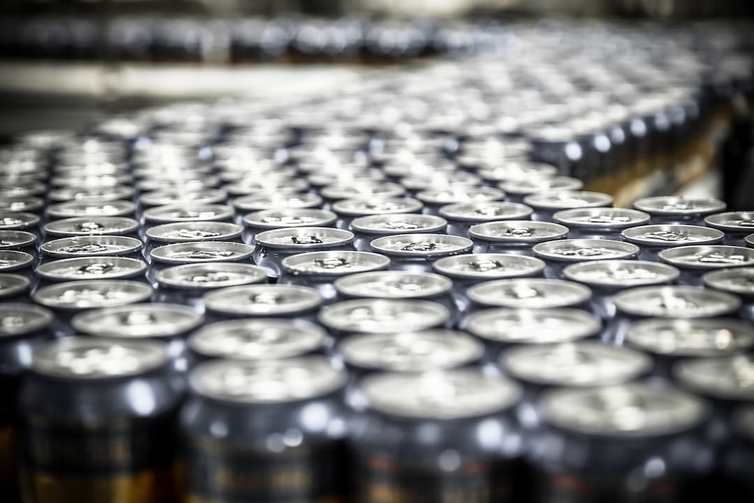 A row of beer cans moving along a conveyor belt in a production facility, showcasing the can manufacturing process.